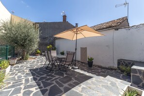 An outdoor patio with stone flooring, a table with chairs, and a large umbrella. - Tourist Home 'La Posada del Pueblo', Sotillo de las Palomas (Sotillo de las Palomas)