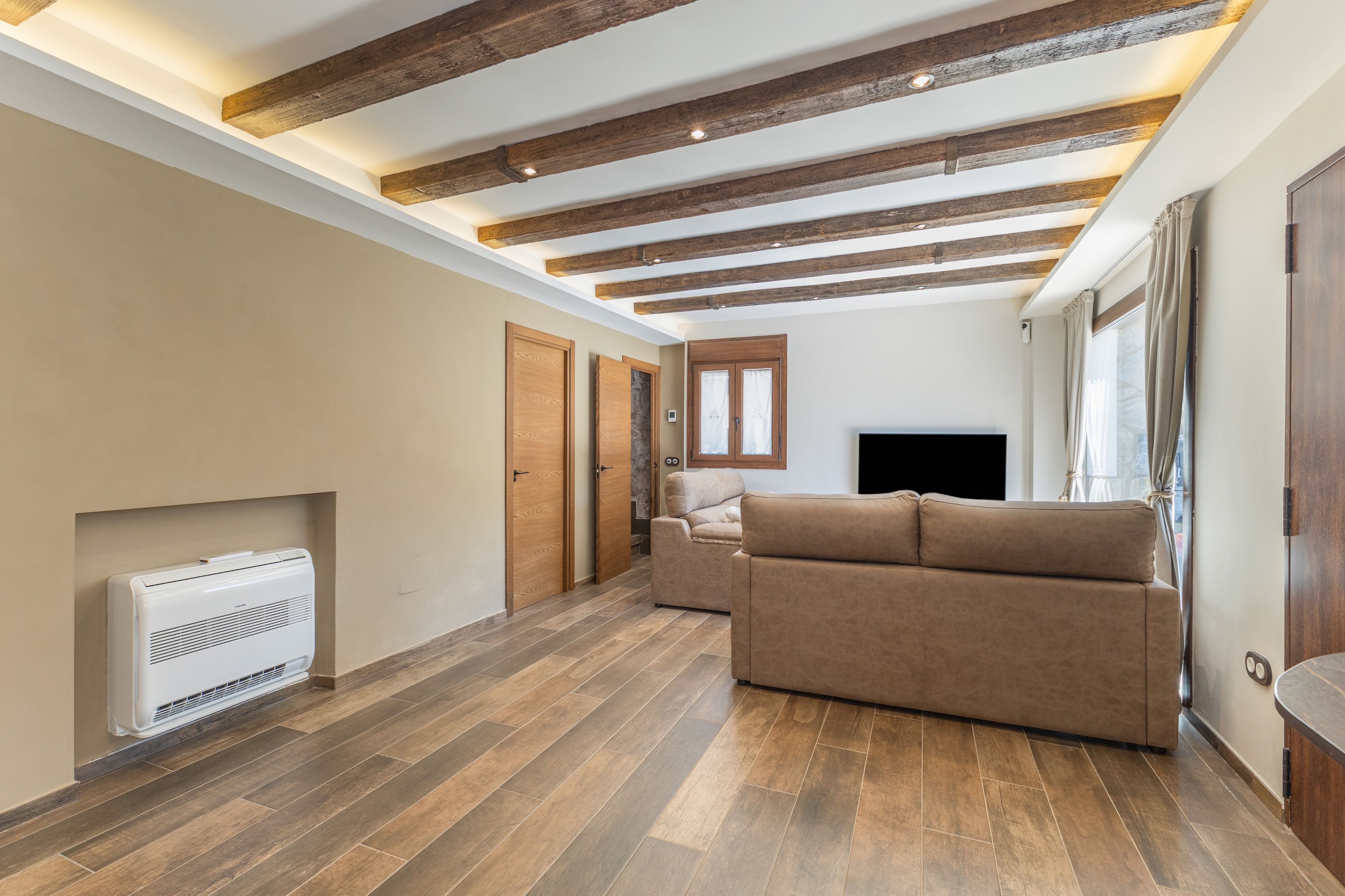 Un espacio habitable amplio con techo de madera, un televisor de pantalla plana, un sofá beige y una chimenea.