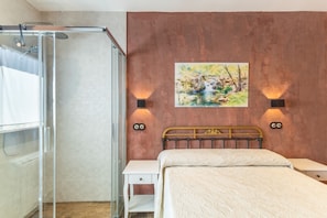 A bedroom with a bed, a nightstand, a wall-mounted painting, and a shower area. - Rural House 'Casa Rural con Piscina Privada en Sotillo de las Palomas, Sierra de Gredos' (Sotillo de las Palomas)