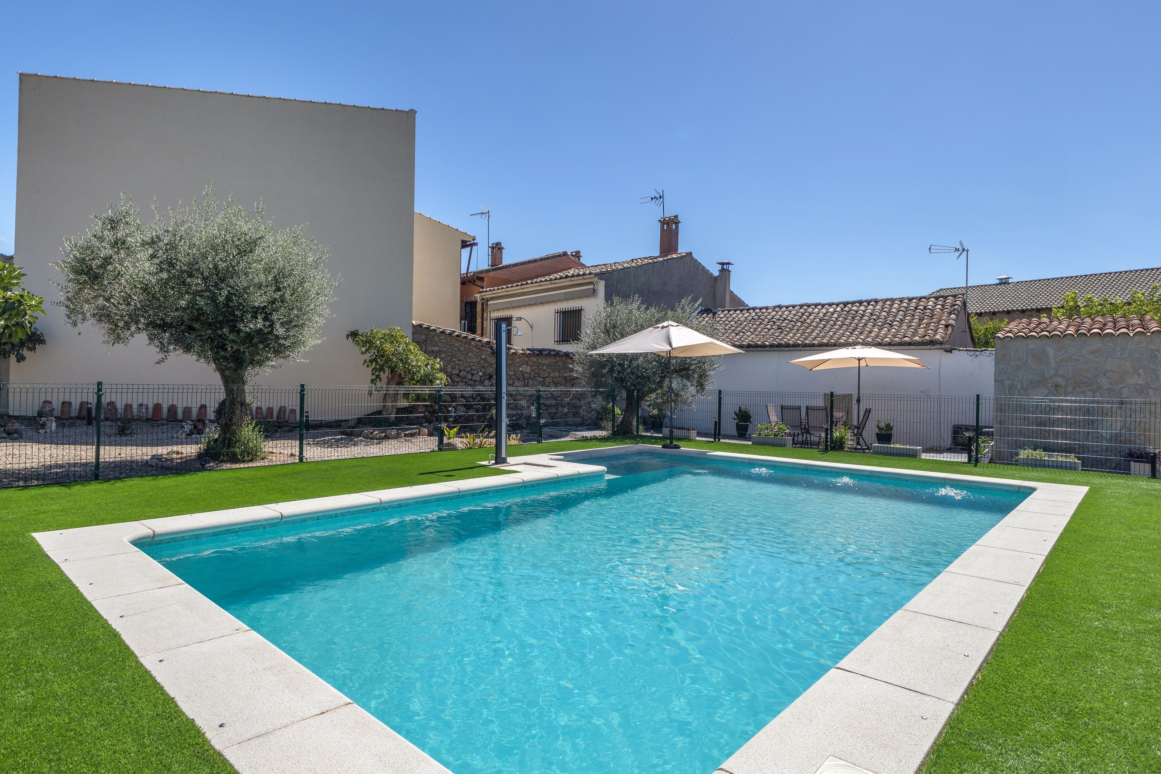 Una piscina rectangular con borde de piedra, rodeada por un césped cuidado y una cerca.