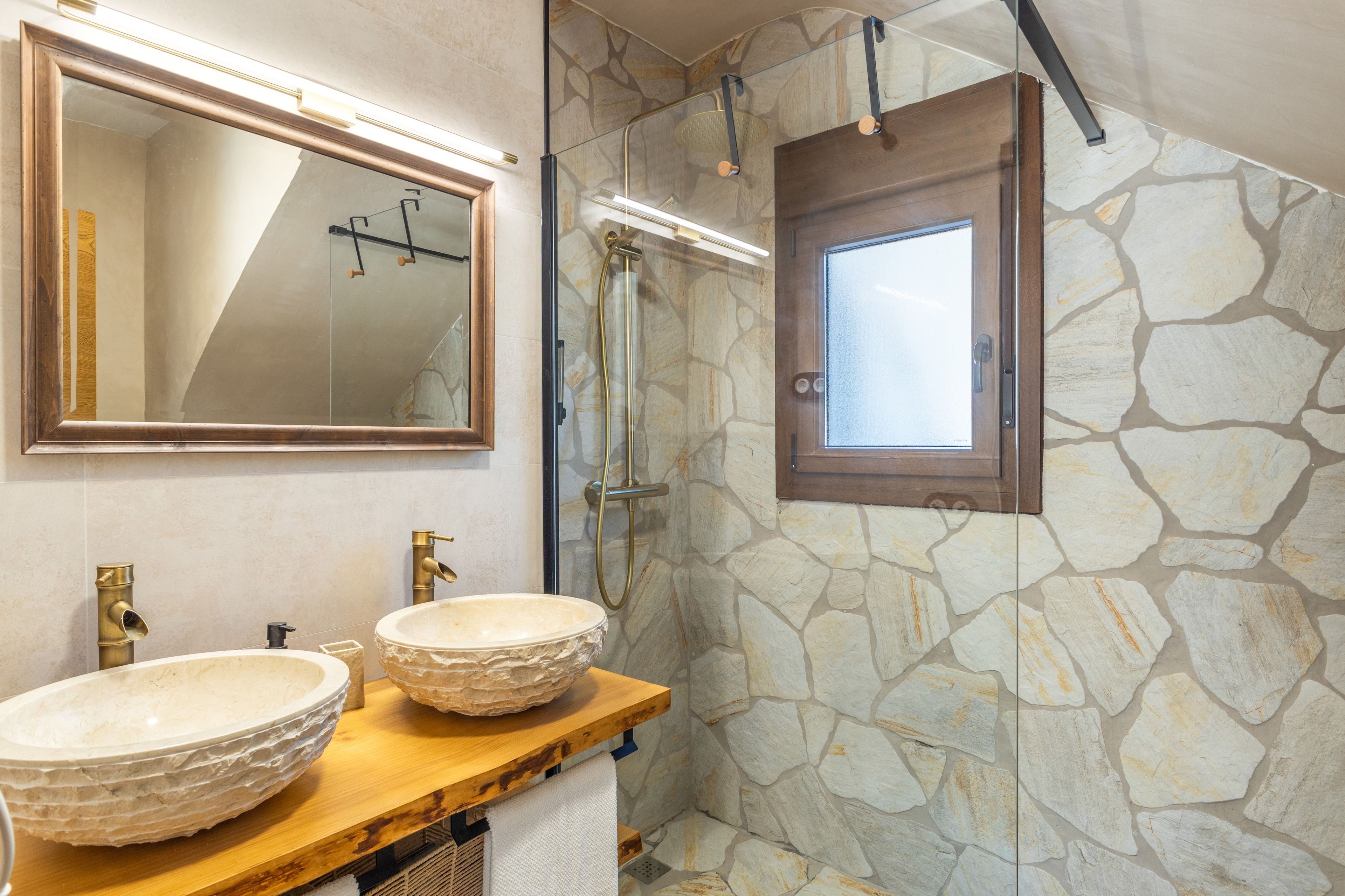 Une salle de bain avec deux vasques en pierre, un miroir et un espace douche.