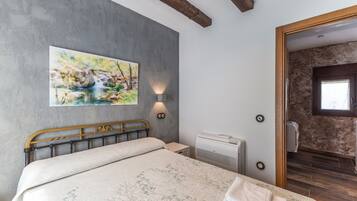 Un dormitorio con cama, un cuadro, una lámpara de pared, unidad de aire acondicionado y una puerta de madera que da a otra habitación.
