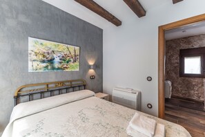 Een slaapkamer met een bed, een schilderij, een wandlamp, een airconditioningapparaat en een houten deur die naar een andere kamer leidt.