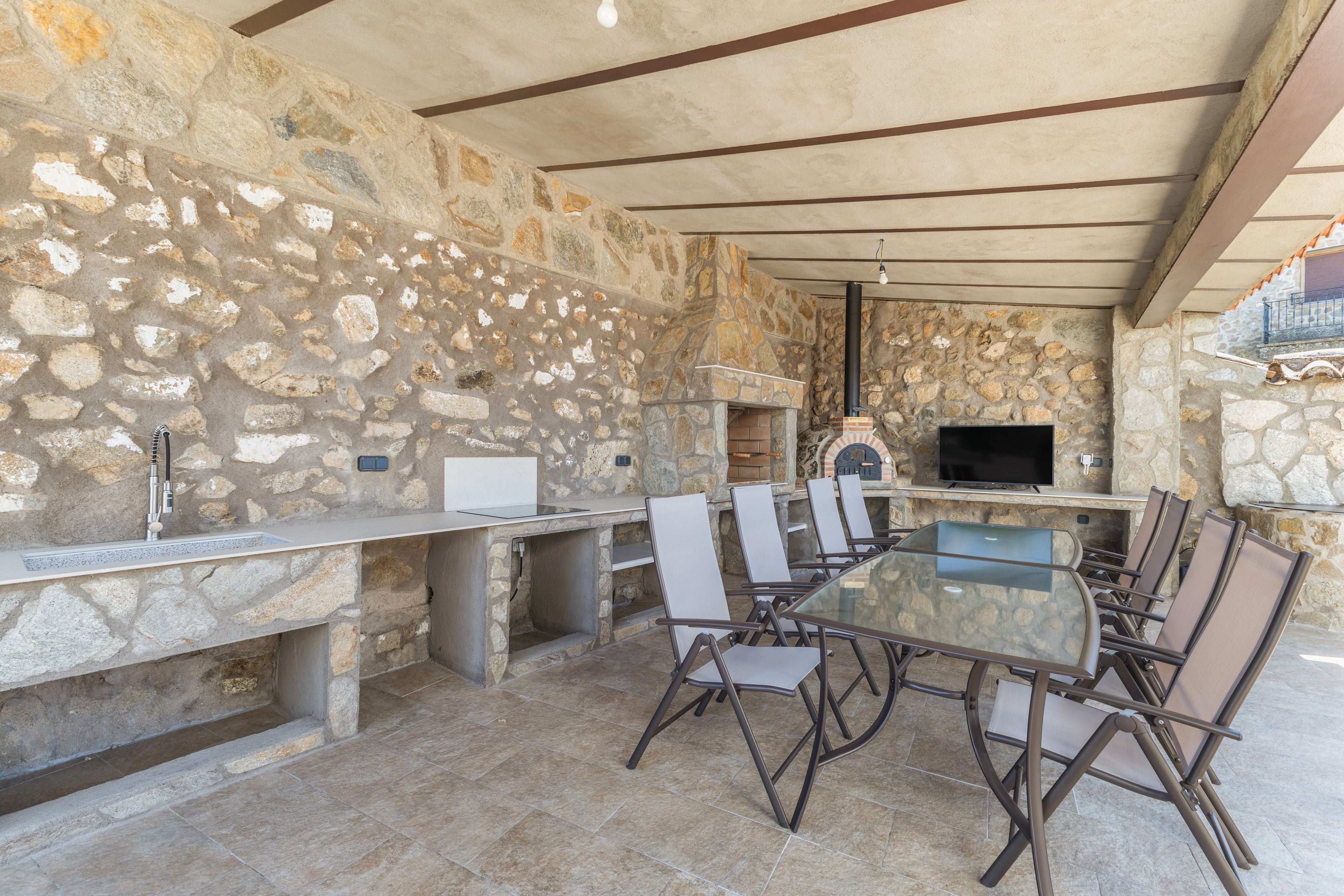 Un área de comedor al aire libre con paredes de piedra, una parrilla empotrada y un televisor de pantalla plana.