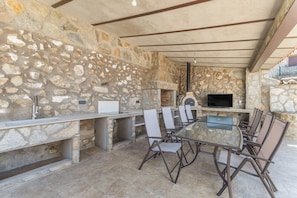 Un área de comedor al aire libre con paredes de piedra, una parrilla empotrada y un televisor de pantalla plana.