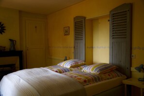 Ein Zimmer mit einem Bett, einem Nachttisch, einer Lampe, einer Tür und einer Wand mit einem Bild.