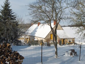 Eine verschneite Landschaft mit einem Haus, einem Holzstapel und einem Stacheldrahtzaun.