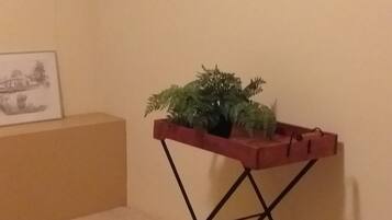 Une pièce avec un lit, une petite table sur laquelle se trouve une plante, un tableau accroché au mur et un chapeau suspendu au mur.