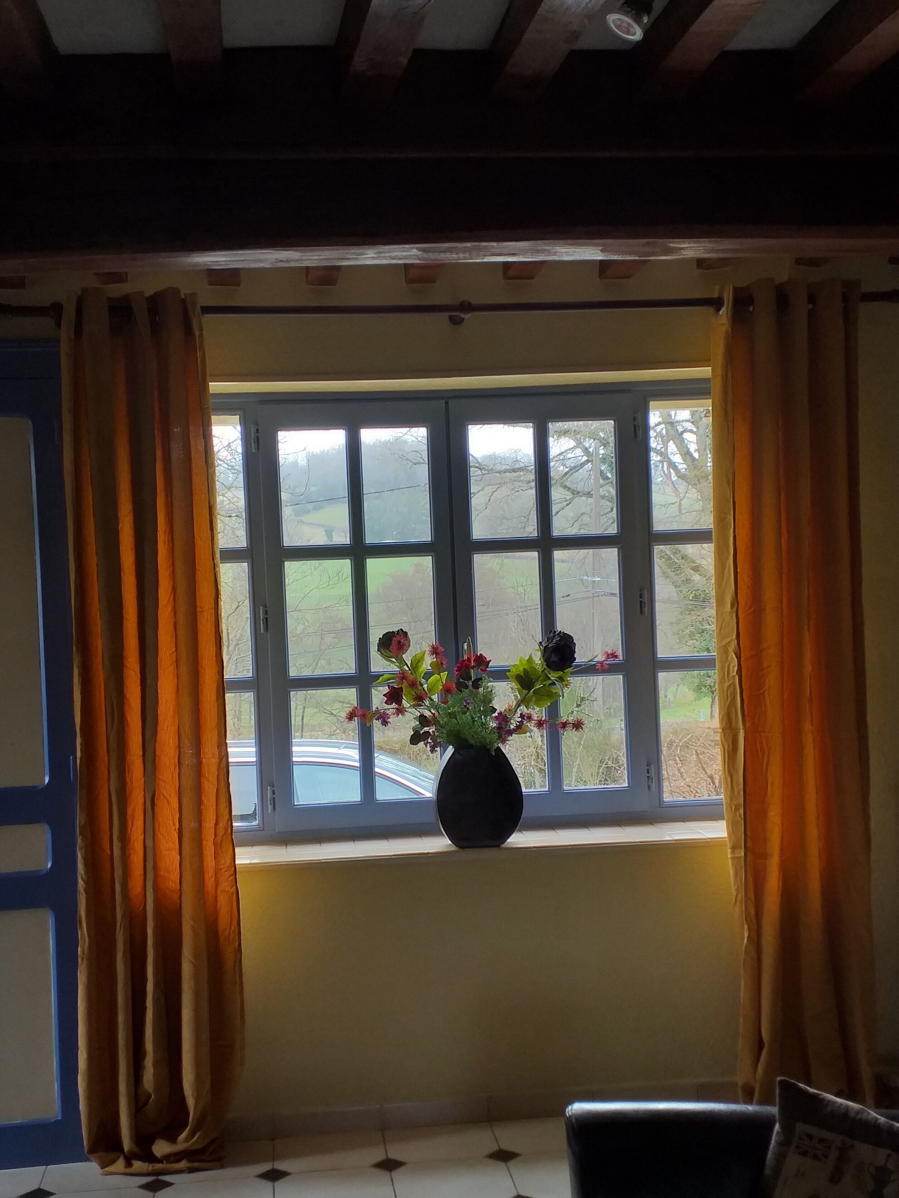 Een kamer met raam, gordijnen en een bloemenvaas.