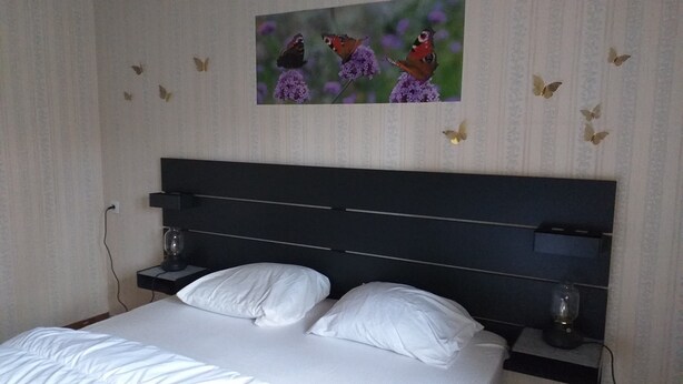 Un dormitorio con una cama, dos mesitas de noche, una obra de arte en la pared y adhesivos decorativos de mariposas.
