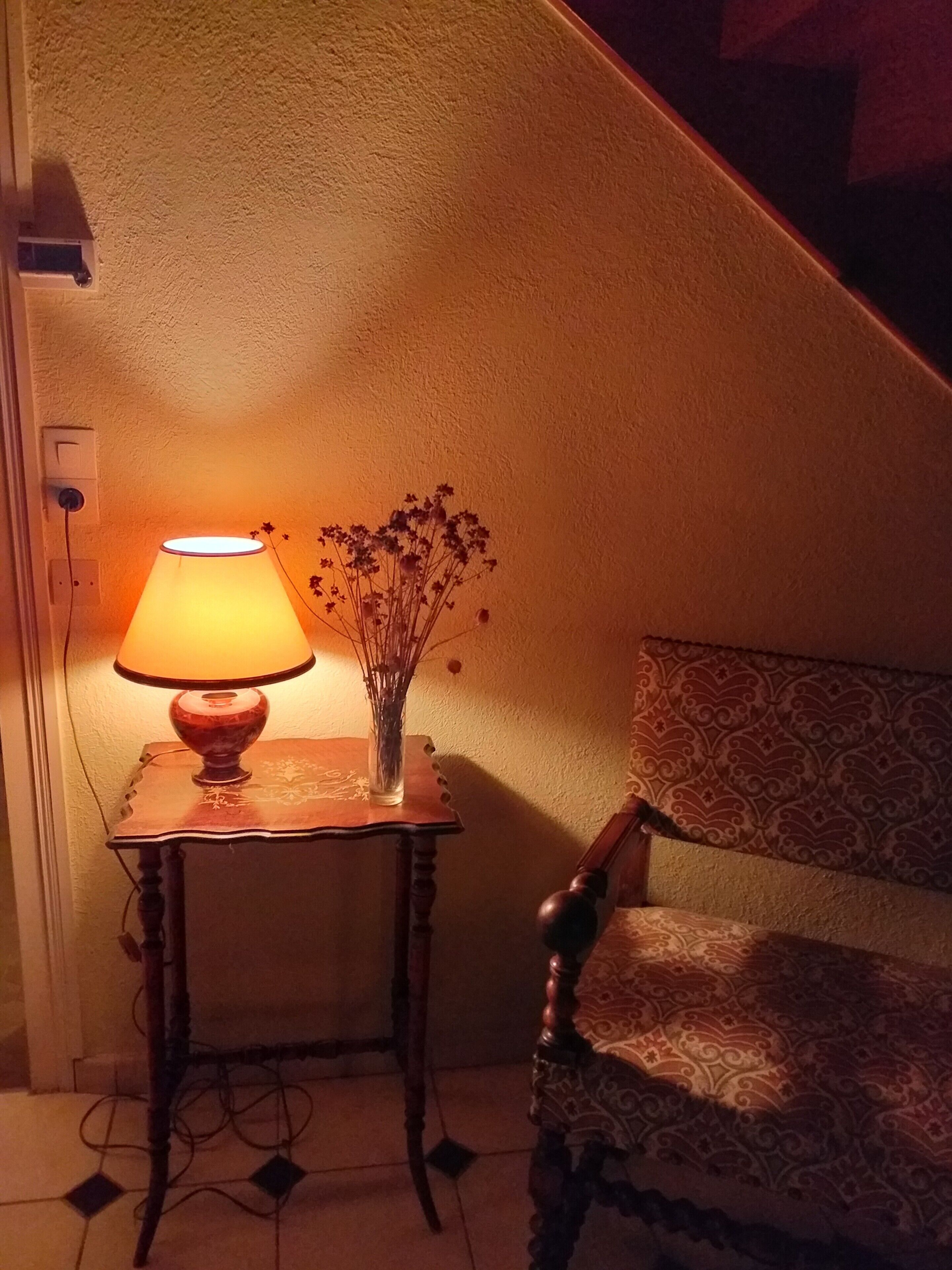 En lampe på et lille bord ved siden af en stol med en mønstret pude.