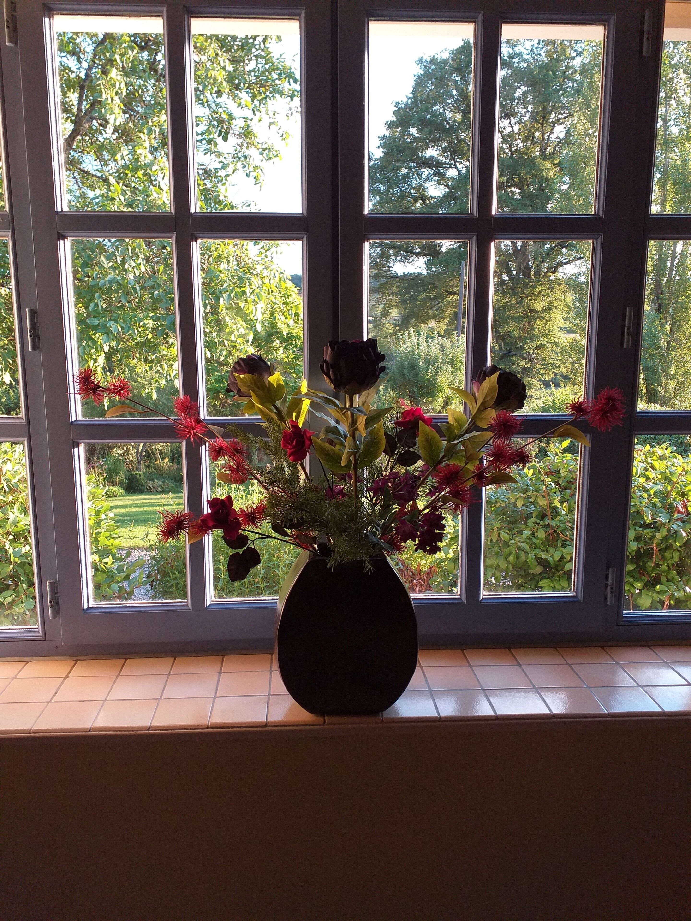 A window with a view of greenery and a vase with flowers on a windowsill.