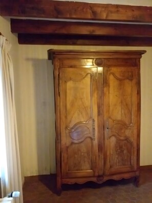 A wooden wardrobe with a classic design, positioned in a room with a tiled floor and a wooden ceiling.