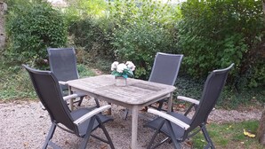 Una mesa redonda de madera con cuatro sillas, rodeada de grava, y un arreglo floral sobre la mesa.