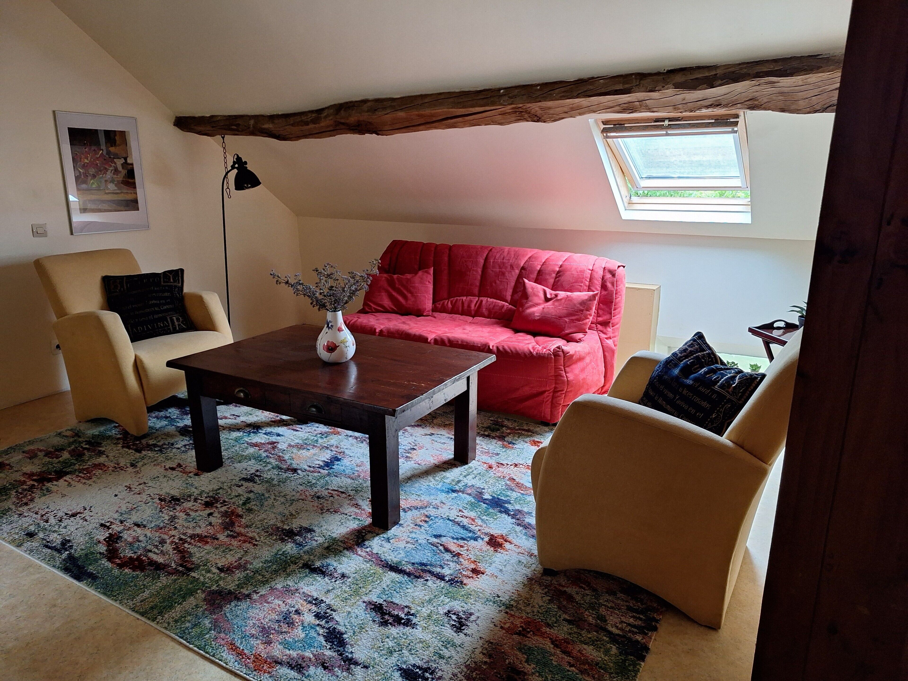 Un salon chaleureux avec un canapé rouge, des fauteuils beiges, une table basse en bois et un tapis coloré.