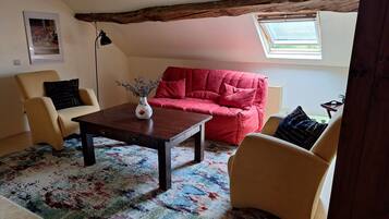 Un salon chaleureux avec un canapé rouge, des fauteuils beiges, une table basse en bois et un tapis coloré.