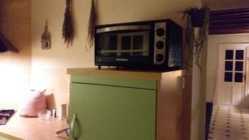 A kitchen with a microwave on a green cabinet, a checkered cloth, and a window with a patterned view.