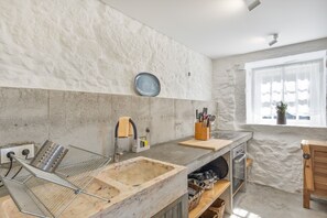 A modern kitchen with a marble countertop, a built-in oven, and a window with a view. - Casa do Gasparinho: Mountain View, Shared Pool & Wi-Fi (Sandiães)