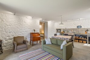 A cozy living room with a sofa, armchair, and a colorful striped rug. - Casa do Gasparinho: Mountain View, Shared Pool & Wi-Fi (Sandiães)