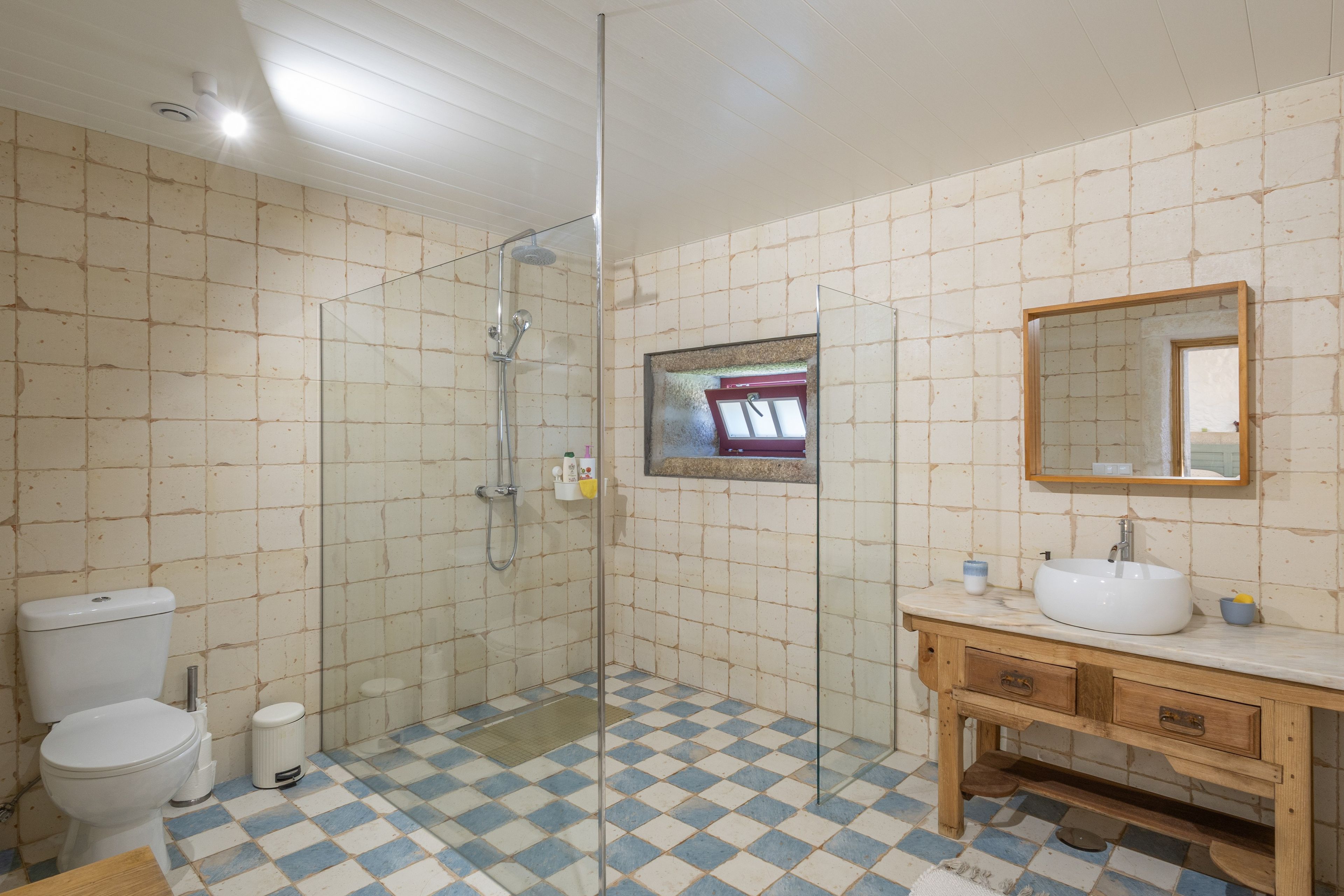 Ein Badezimmer mit einer Duschkabine aus Glas, einer weißen Toilette, einem Waschbecken mit Spiegel darüber und einem Schachbrettboden.