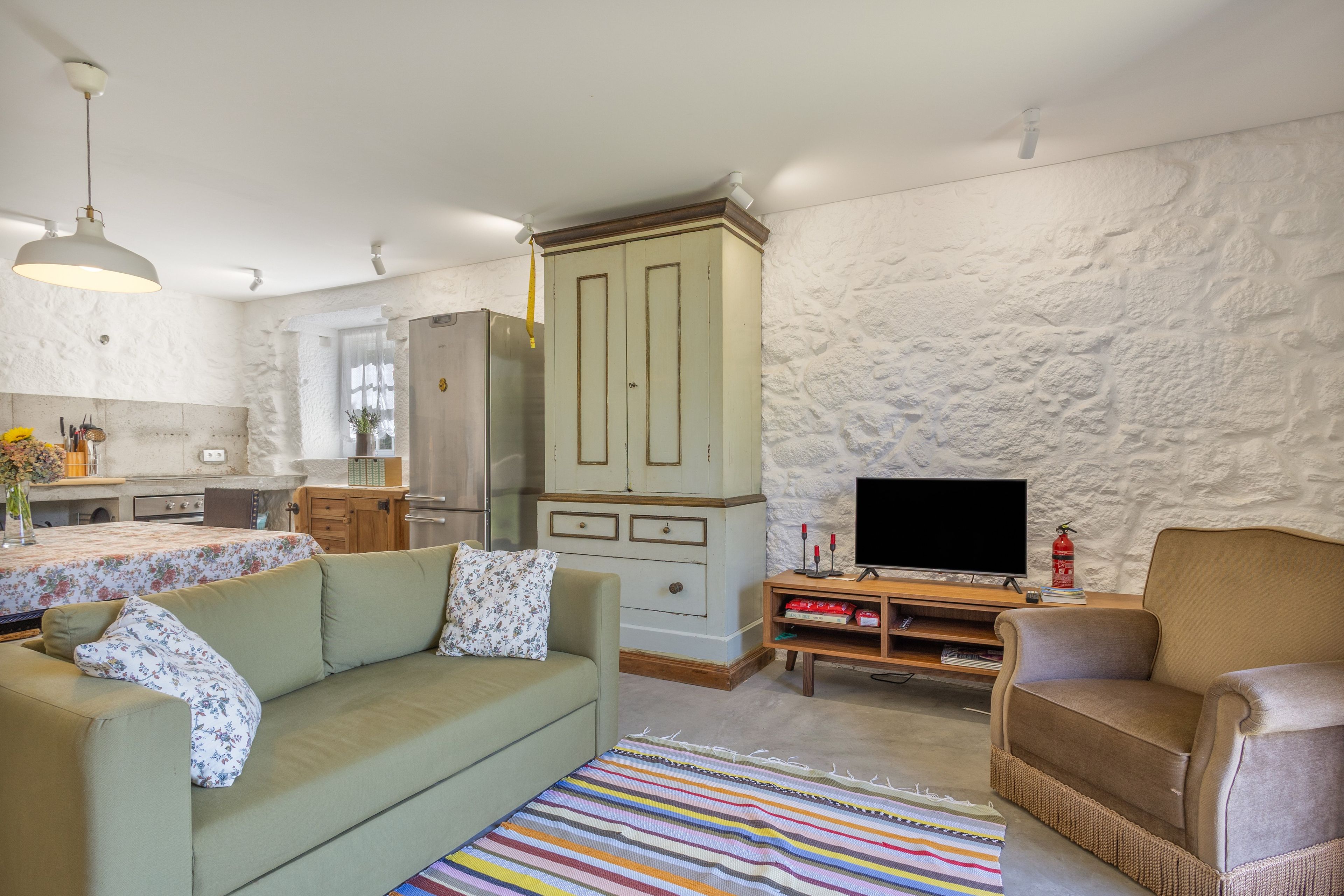 A living room with a sofa, a television, a fireplace, and a kitchen area in the background.