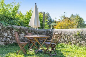 A table and chairs set outdoors with a stone wall backdrop and greenery. - Casa do Gasparinho: Mountain View, Shared Pool & Wi-Fi (Sandiães)