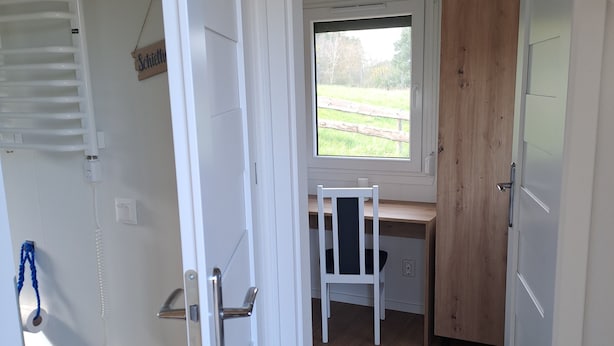 A room with a wooden desk, a chair, a window with a view of a grassy field, and a white radiator.