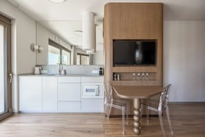 A modern kitchen with a built-in TV, wooden cabinets, and a clear glass dining table. - LILY ART with wine - Gdansk Shipyard & Rooftop Terrace by Lily Apart (GdaĆsk)