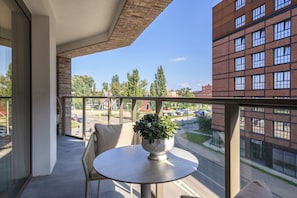 Ein Balkon mit Tisch und Stühlen, einem Blumentopf und Blick auf einen Parkplatz sowie Gebäude.