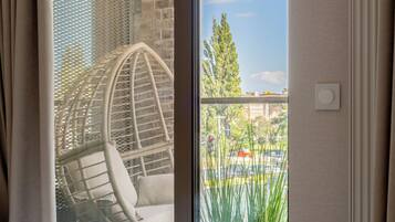 A hotel room with a bed, a wicker chair, and a view of the street and buildings outside.