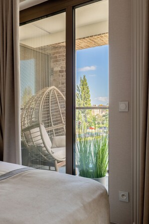 A hotel room with a bed, a wicker chair, and a view of the street and buildings outside. - LILY ART with wine - Gdansk Shipyard & Rooftop Terrace by Lily Apart (GdaĆsk)