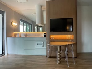 A modern kitchen with a built-in TV, a dining area with a clear chair, and a large window. - LILY ART by Lily Apart (Gdańsk)