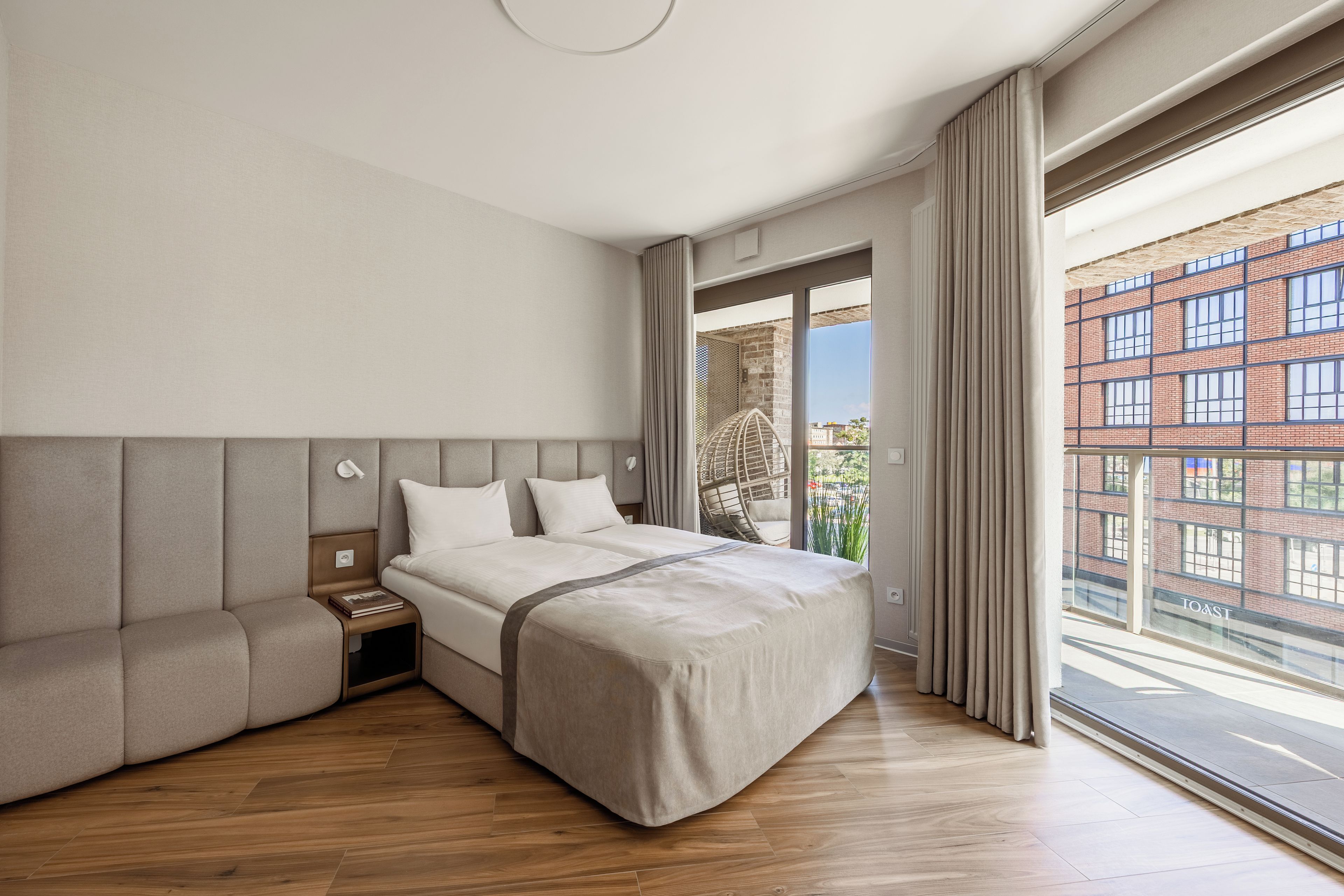 Habitación de hotel moderna con una cama grande, un sofá, una mesita de noche y vistas a un edificio a través de la ventana.