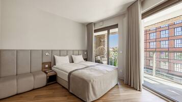 Habitación de hotel moderna con una cama grande, un sofá, una mesita de noche y vistas a un edificio a través de la ventana.