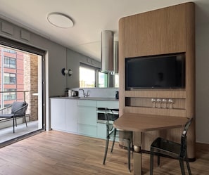 A modern kitchen with a built-in TV, wooden cabinetry, and a dining area with chairs. - LILY ART by Lily Apart (Gdańsk)