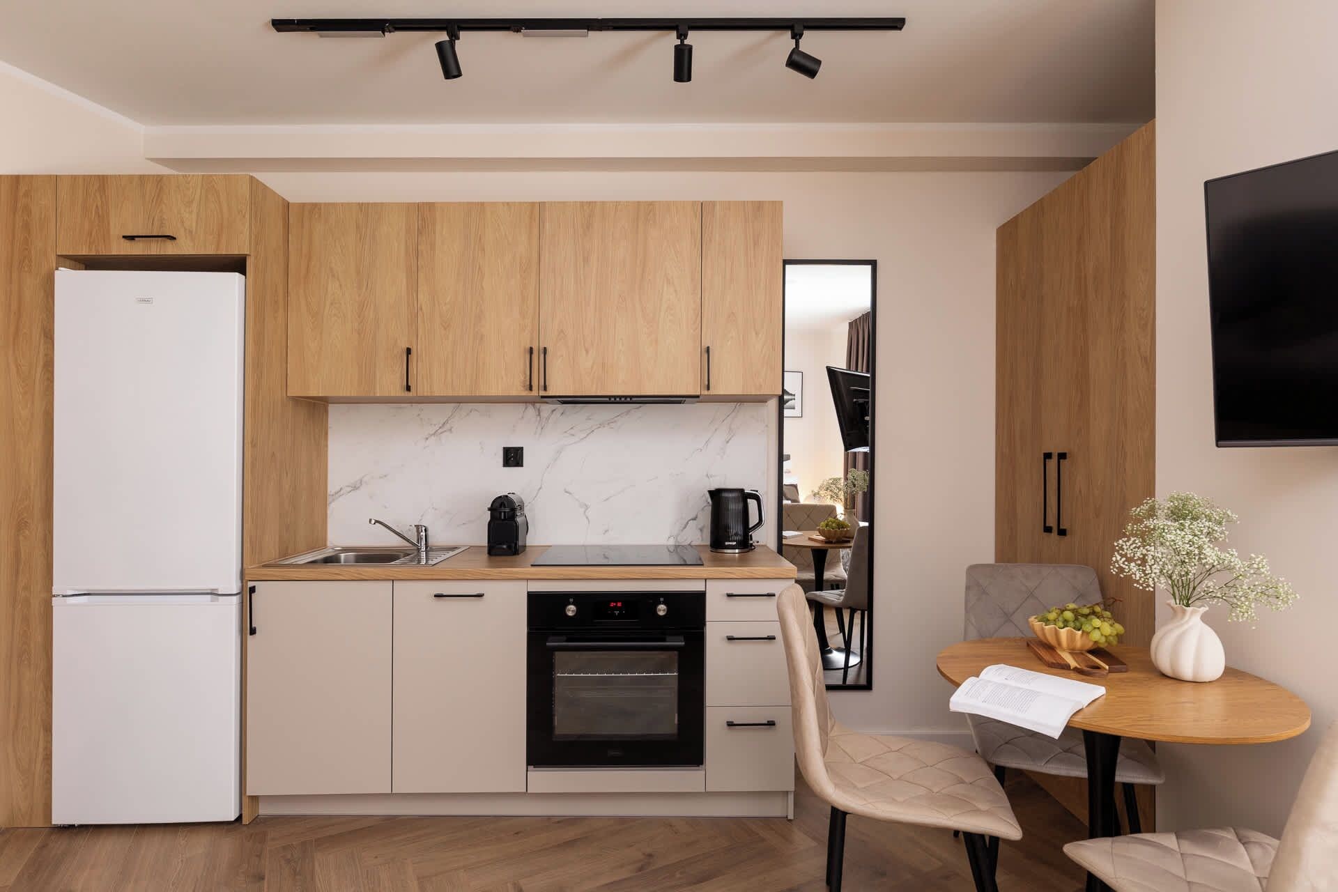 A modern kitchen with wooden cabinets, a built-in oven, and a dining area with a table and chairs.