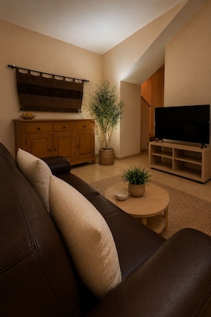 Una sala de estar con sofá, televisor, aparador y planta.