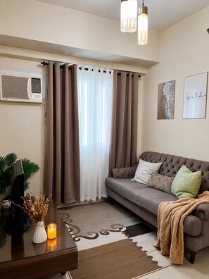 Ein Wohnzimmer mit einem grauen Sofa, einem kleinen Tisch mit einer Kerze und einer Wand-Klimaanlage.