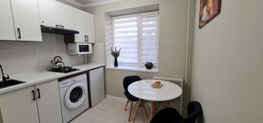 Cocina compacta con lavadora, microondas y ventana con persianas.