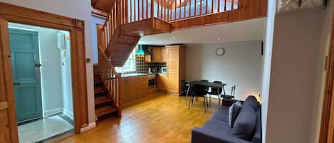 A spacious living area with a wooden staircase, a kitchen, and a dining area.