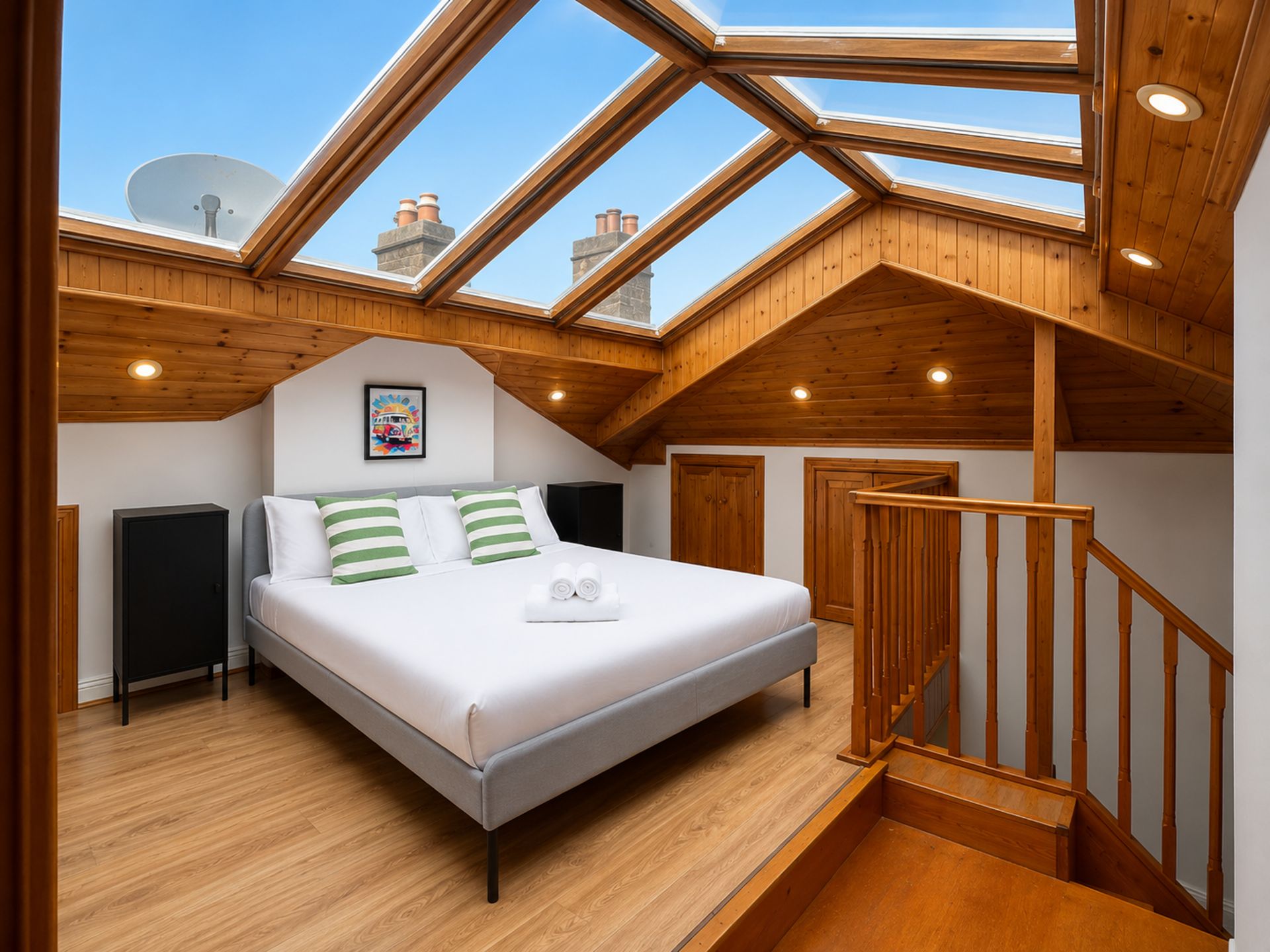 A bedroom with a skylight, wooden beams, a bed with pillows, and a small bedside table.