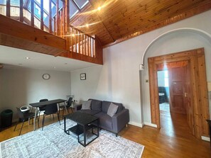 A spacious living area with a high ceiling, wooden beams, a dining table with chairs, a sofa, and a patterned rug. - Characterful 1BDR Cottage with Loft in Dublin (Dublin)