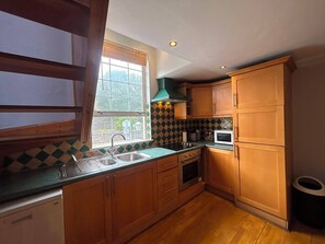 A compact kitchen with wooden cabinets, a stainless steel sink, and a microwave. - Characterful 1BDR Cottage with Loft in Dublin (Dublin)