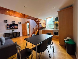 A modern kitchen with a stove, sink, and a window. There is a dining area with a table and chairs. The room has wooden flooring and a staircase.