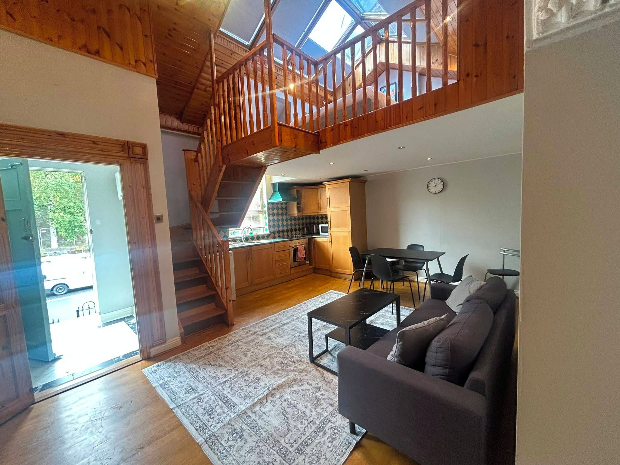 Amplia sala de estar con una escalera que conduce a un altillo, un comedor y una cocina con gabinetes de madera.