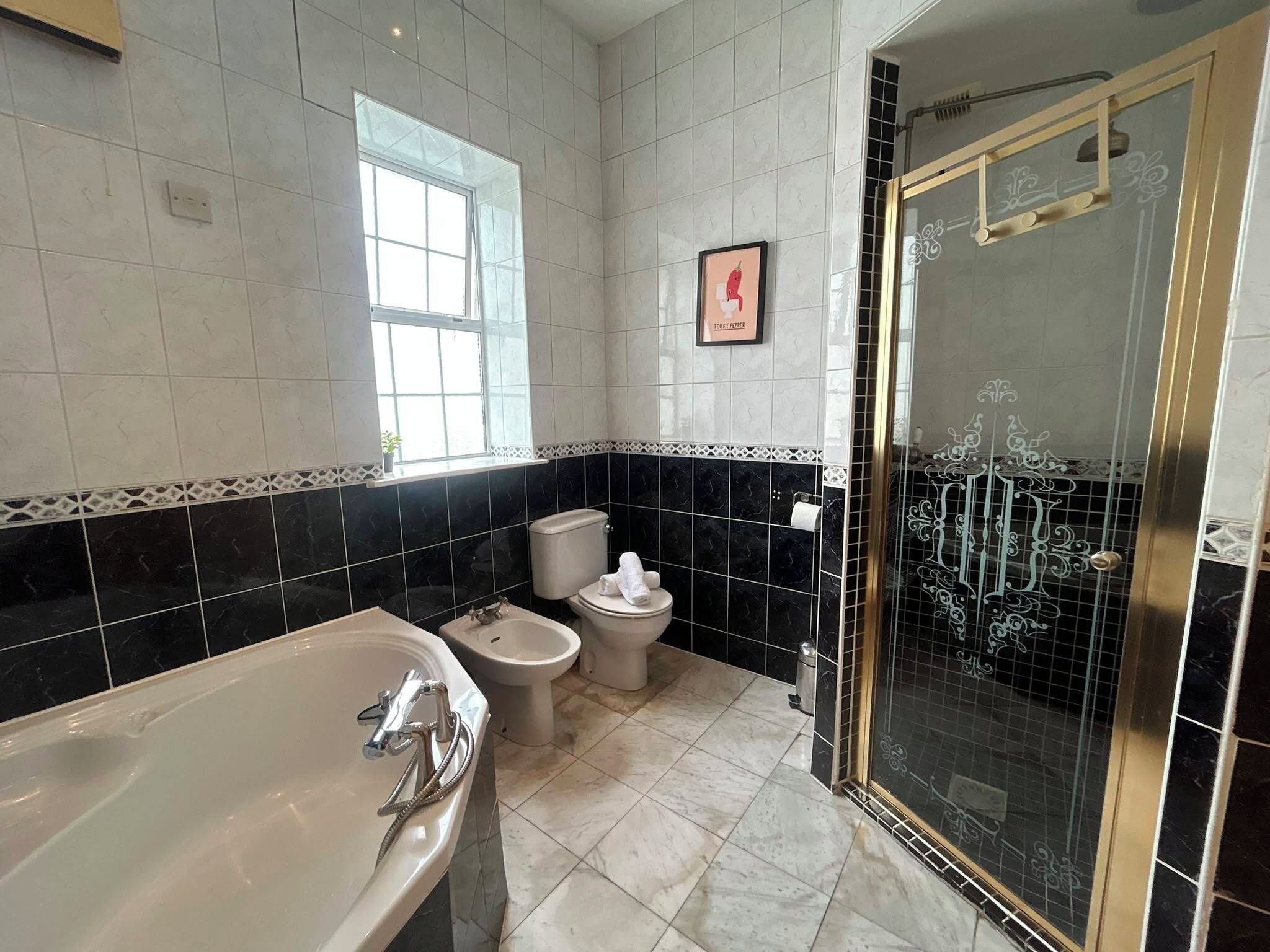 Une salle de bain équipée d’une baignoire, de toilettes, d’un bidet et d’une douche séparée par une paroi en verre.