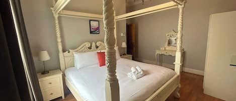 A four-poster bed with a white canopy, a bedside table with a lamp, a mirror, and a picture on the wall.