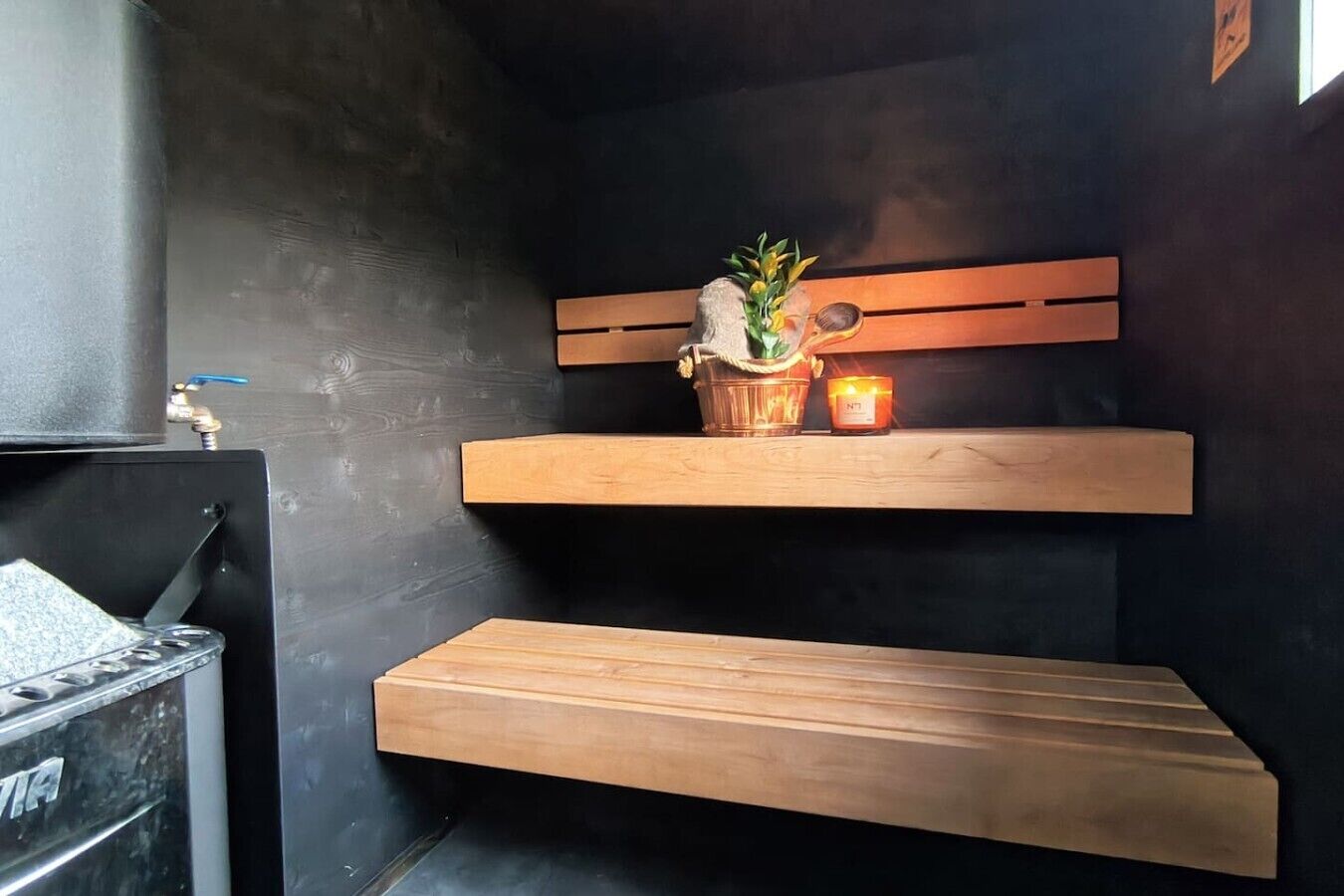 Una habitació amb una paret negra, una cadira de fusta, una taula petita amb una planta i una espelma encès.