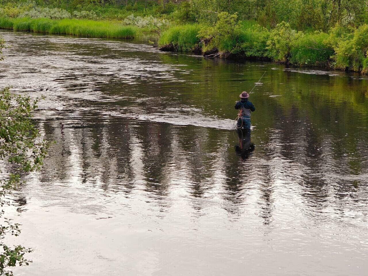 Una persona pesca in un fiume con un paesaggio naturale sullo sfondo.