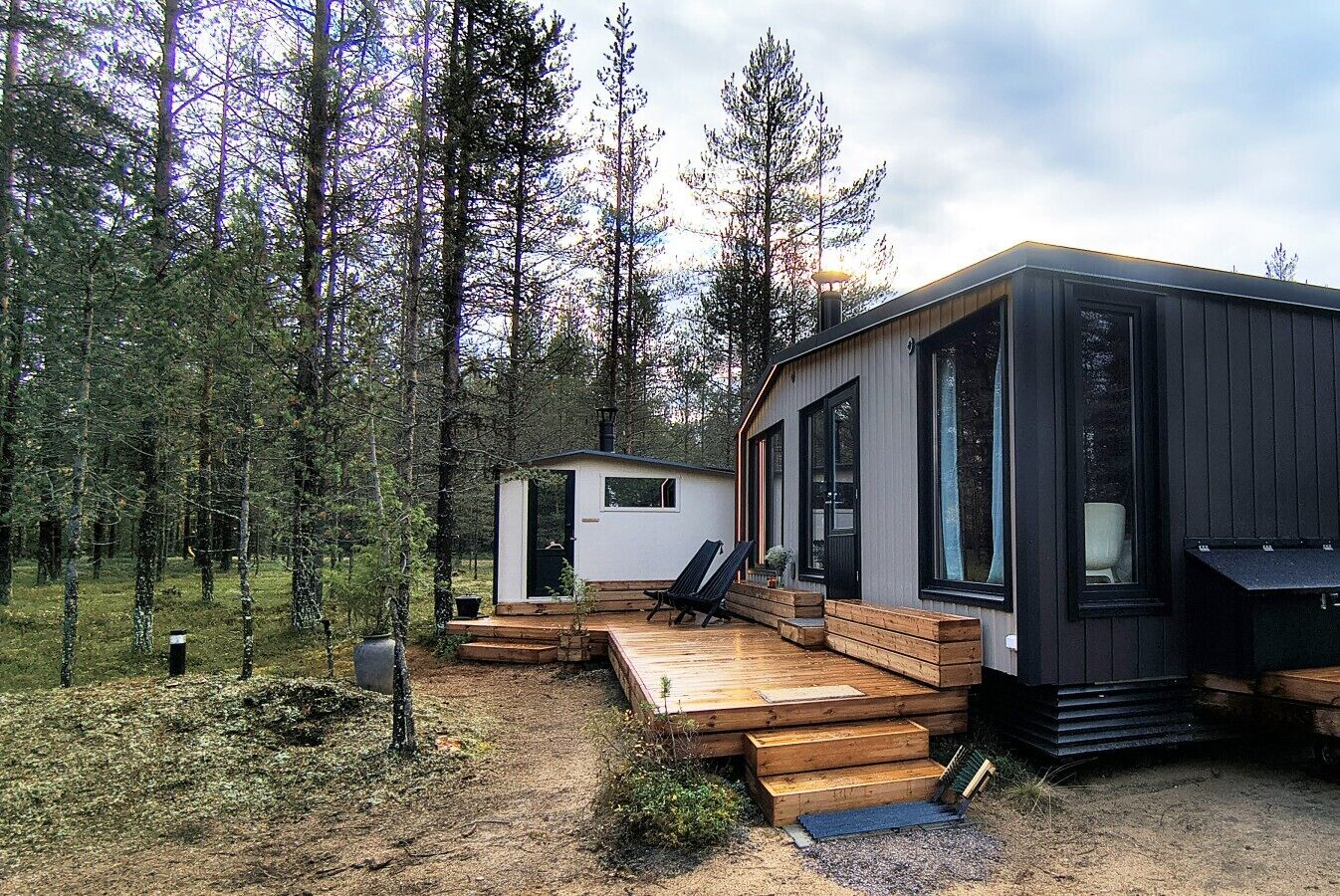 A cabin with a deck, a small shed, and a forested backdrop.